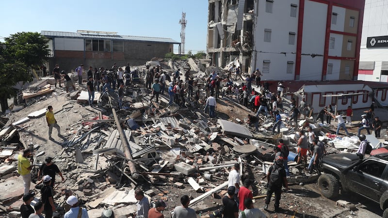 Residentes y equipos de rescate buscan entre los escombros de un edificio derrumbado tras el...