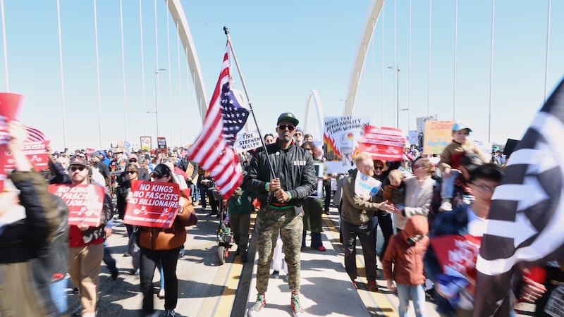 Kymone Freeman sostiene una bandera mientras los manifestantes pasan junto a él por el puente...