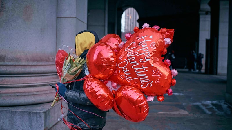 ARCHIVO – Un hombre camina con flores y globos el día de San Valentín, el viernes 14 de...