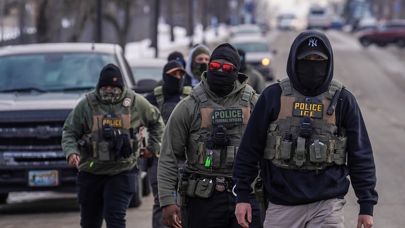 ARCHIVO - Agentes federales caminan por una calle durante un campaña de redadas migratorias el...